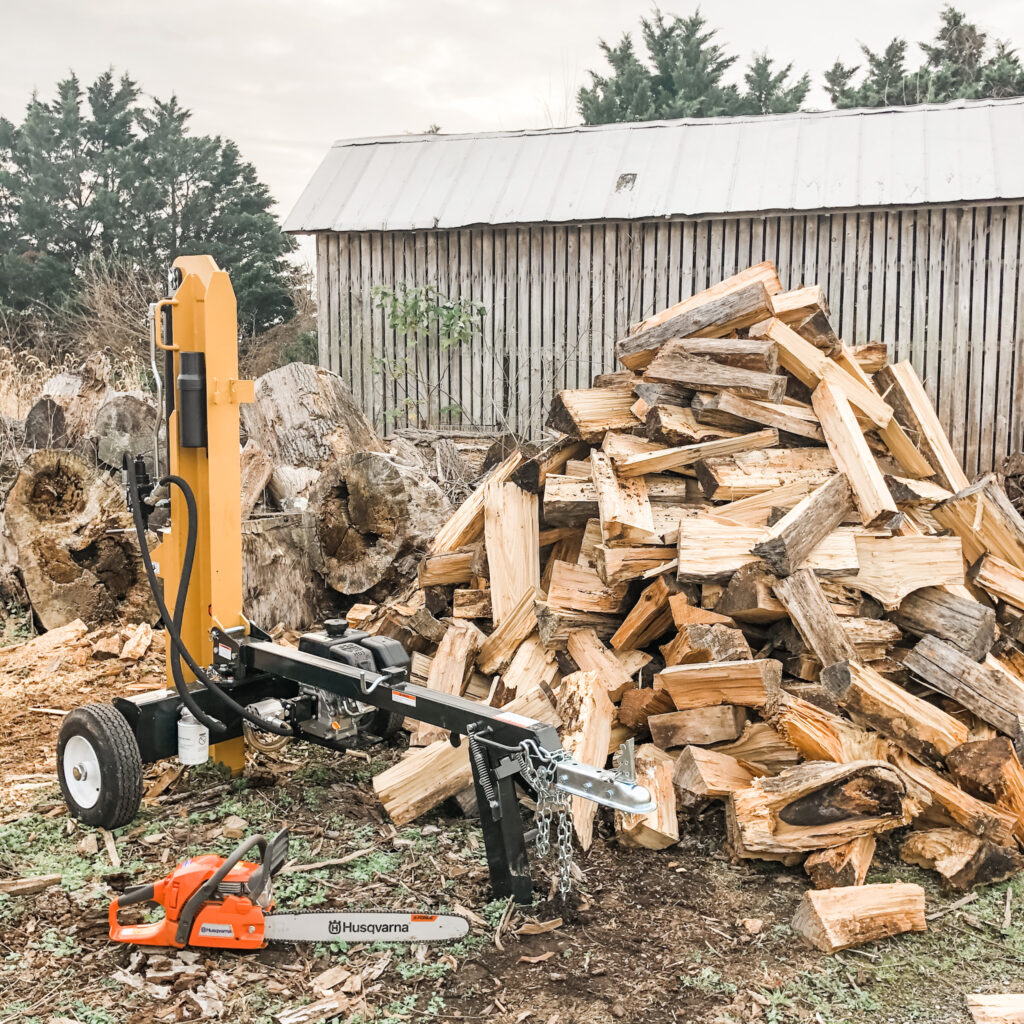 Split wood pile beside a log splitter and a Husqvarna chainsaw