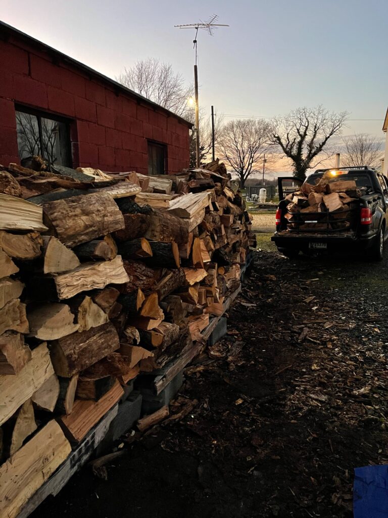 Wood Pile stacked up beside red barn at sunset